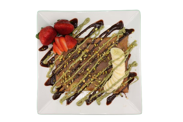 Crepe topped with banana, strawberries, pistachios, and chocolate drizzle