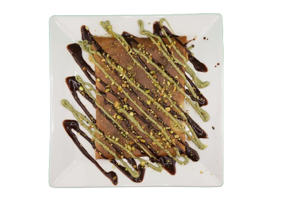 Crepe topped with banana, strawberries, pistachios, and chocolate drizzle